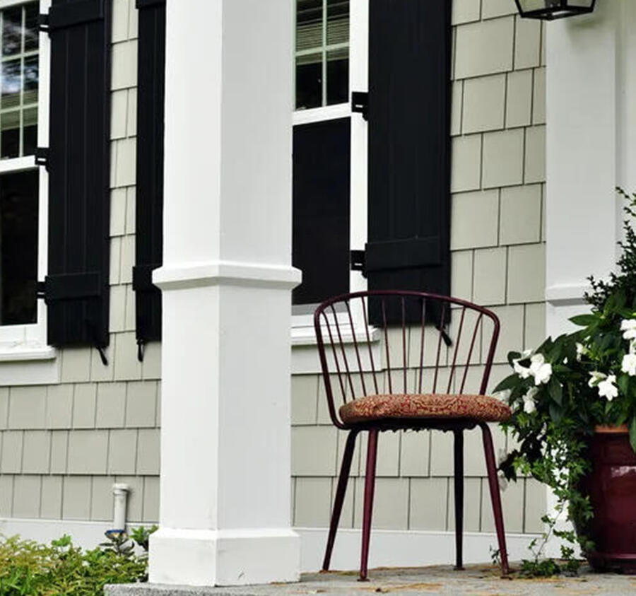 Close-up of a house's exterior corner showing white siding, gutter, and downspout, with green leaves in the background.